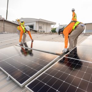 Team technicians carrying photovoltaic solar moduls on roof of factory on the morning. Installing a Solar Cell on a Roof. Solar panels on roof. Workers installing solar cell power plant eco technology.